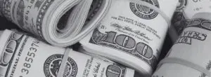 Several rolls of U.S. hundred dollar bills secured with rubber bands, displayed closely together in a black and white image, evoke the high-stakes atmosphere often associated with California sports betting.