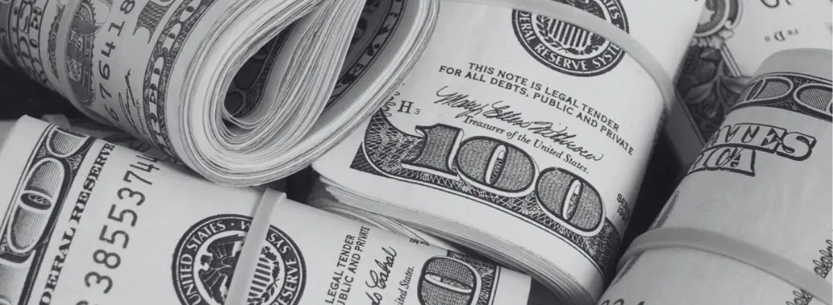 Several rolls of U.S. hundred dollar bills secured with rubber bands, displayed closely together in a black and white image, evoke the high-stakes atmosphere often associated with California sports betting.